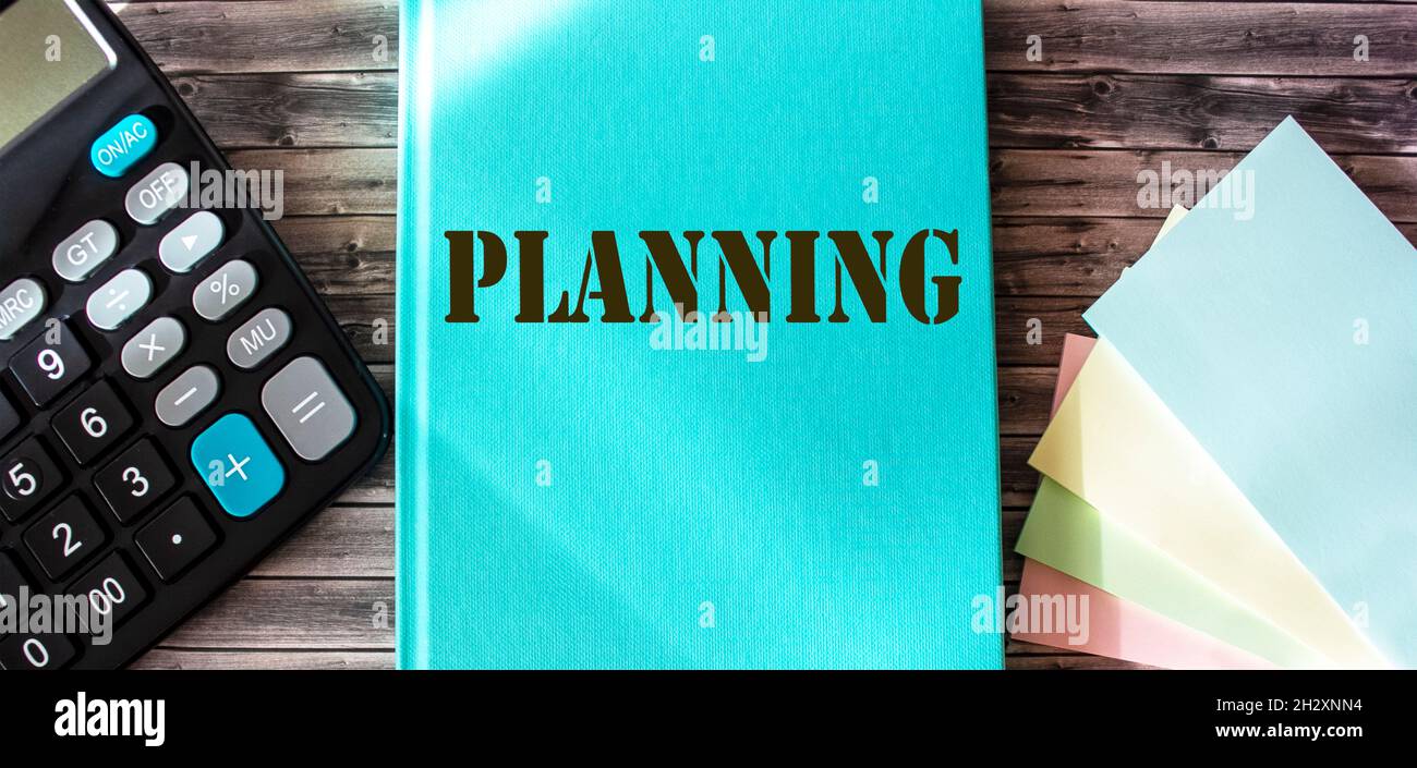 Marketing plan written on a turquoise notepad, office wooden table with a calculator and stickers Stock Photo