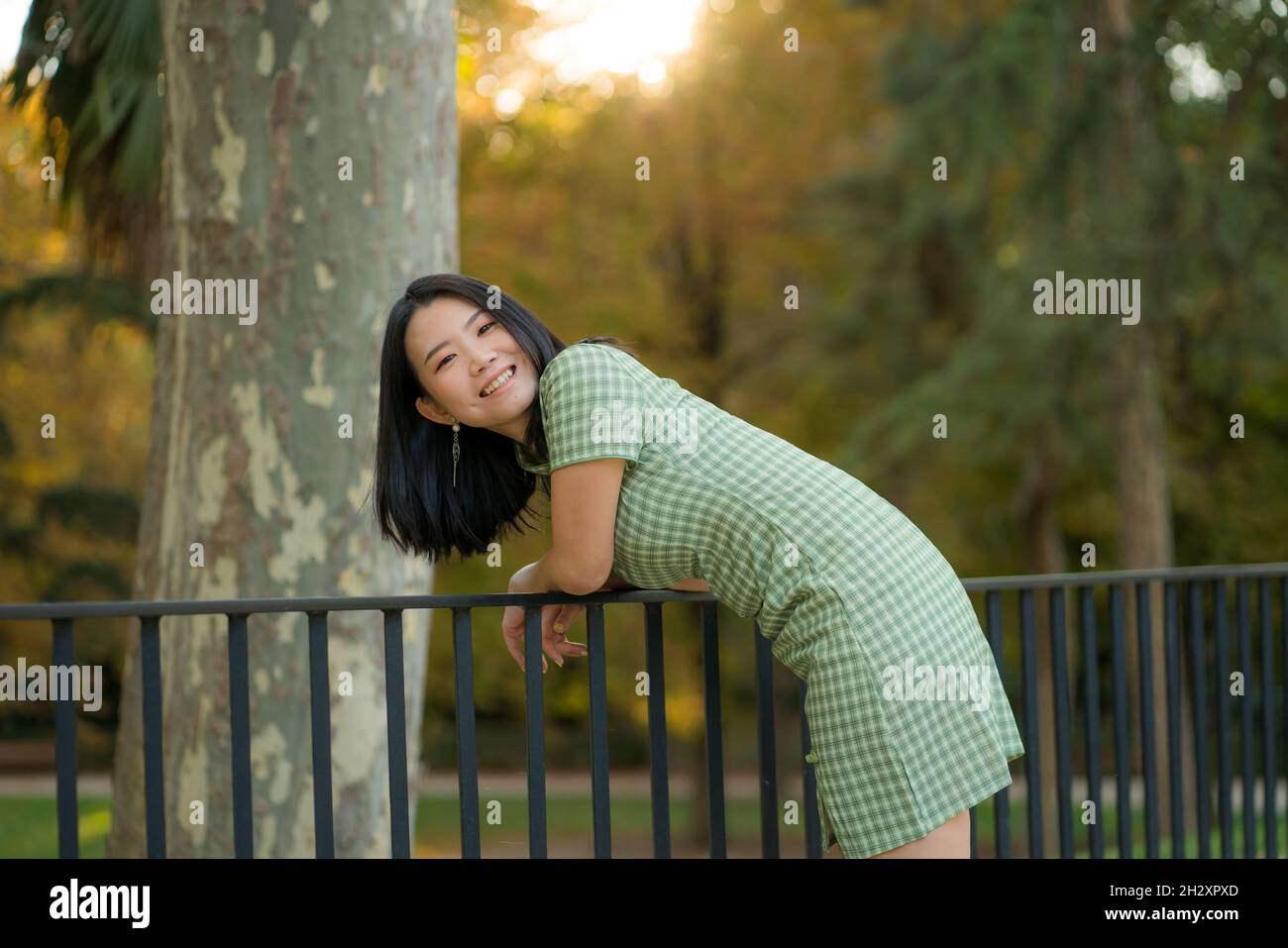 lifestyle portrait of young happy and attractive Korean woman relaxed taking a walk on city park enjoying beautiful sunset dressed in cute Asian dress Stock Photo