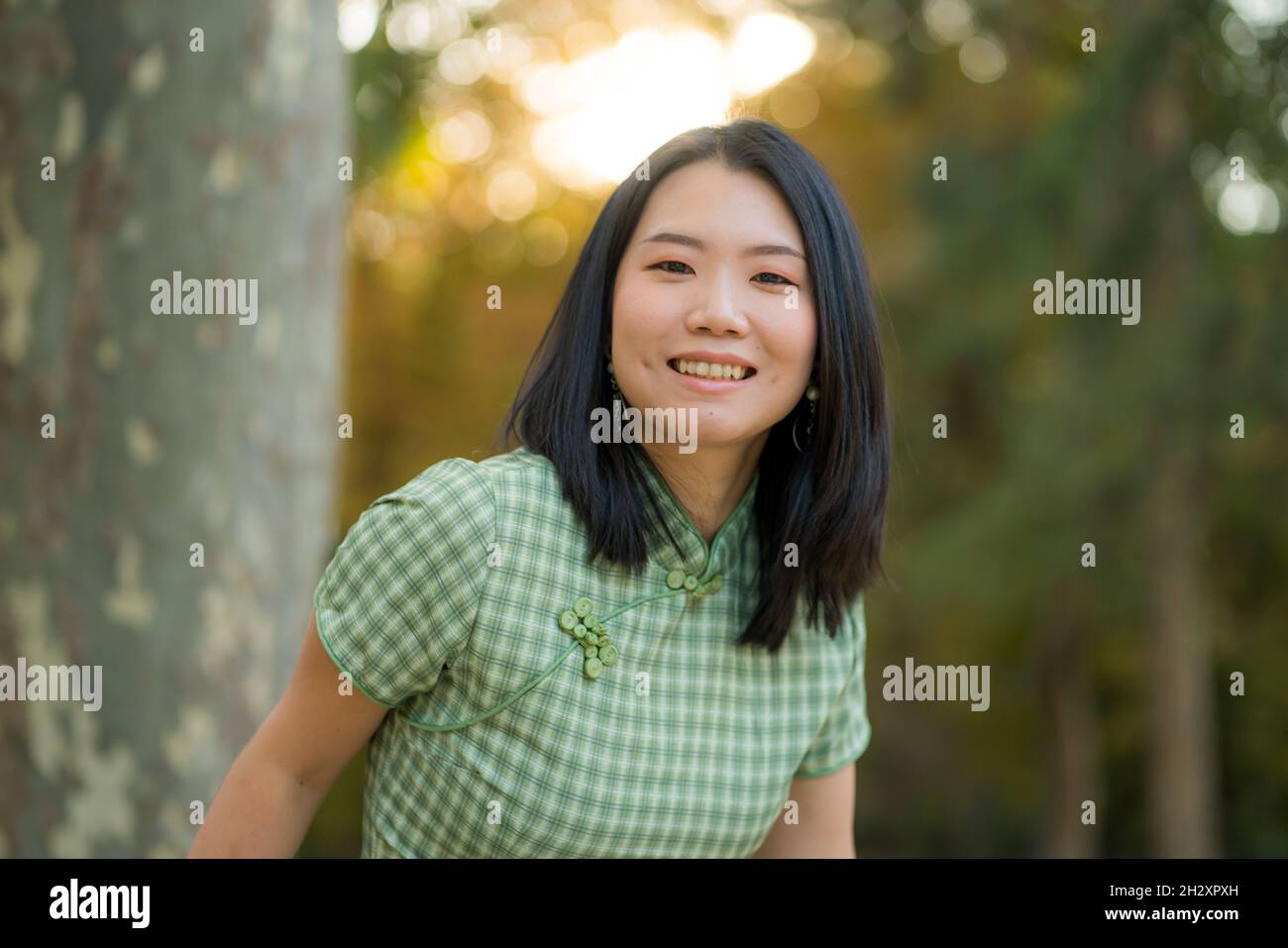 lifestyle portrait of young happy and attractive Korean woman relaxed taking a walk on city park enjoying beautiful sunset dressed in cute Asian dress Stock Photo
