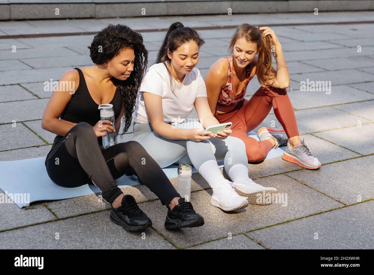 Three sporty women having fun and laughing looking smartphone after urban fitness workout. Stock Photo