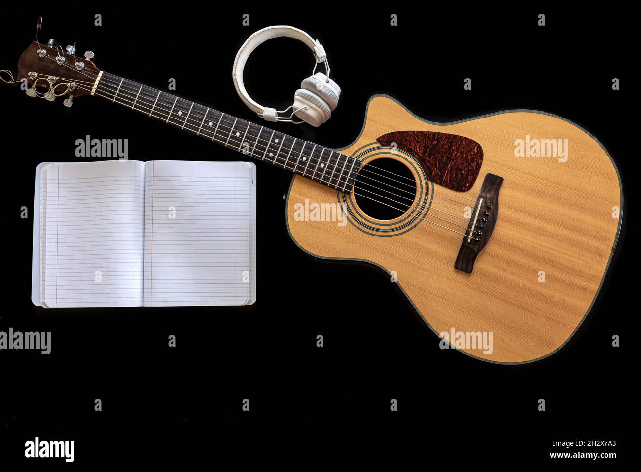 Classical acoustic guitar, headphones and notebook on a black