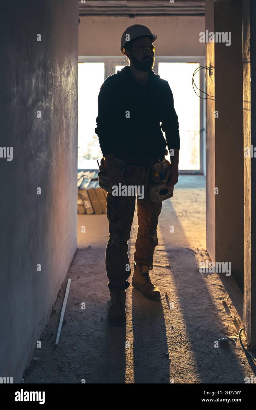 A man builder in work clothes with a protective helmet at a construction site. Stock Photo