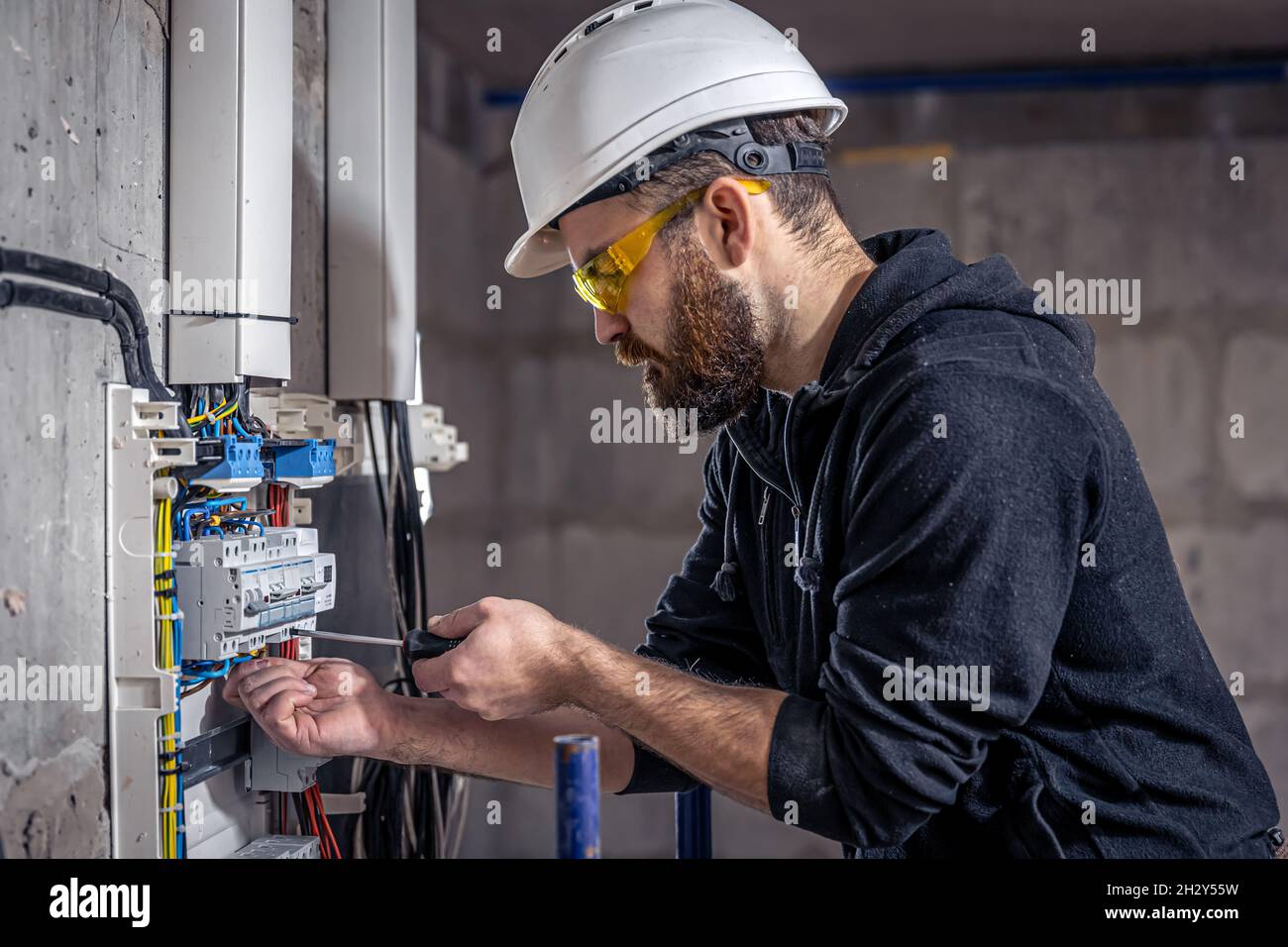 A male electrician works in a switchboard with an electrical connecting cable. Stock Photo