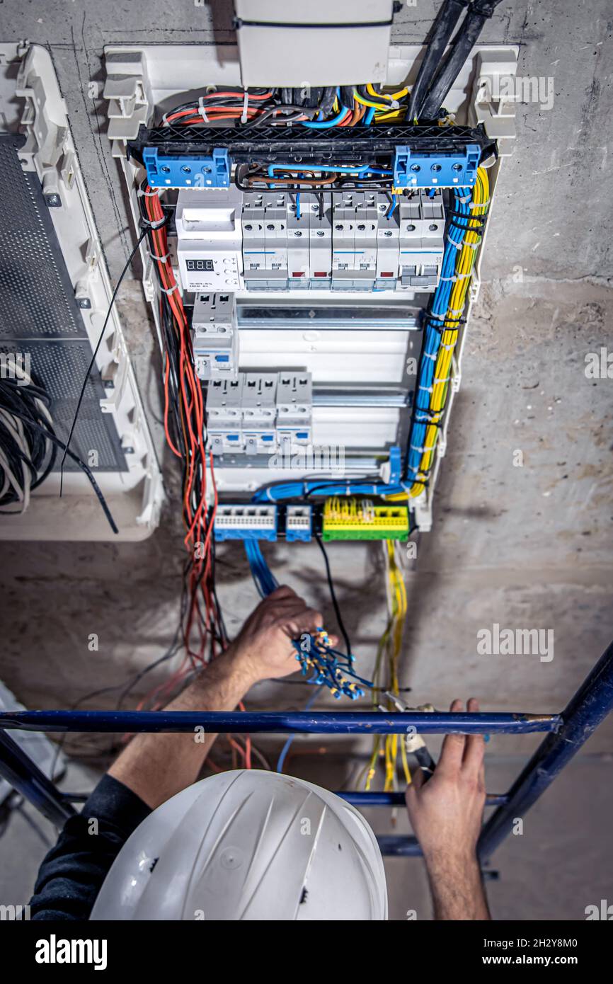 A male electrician works in a switchboard with an electrical connecting cable. Stock Photo