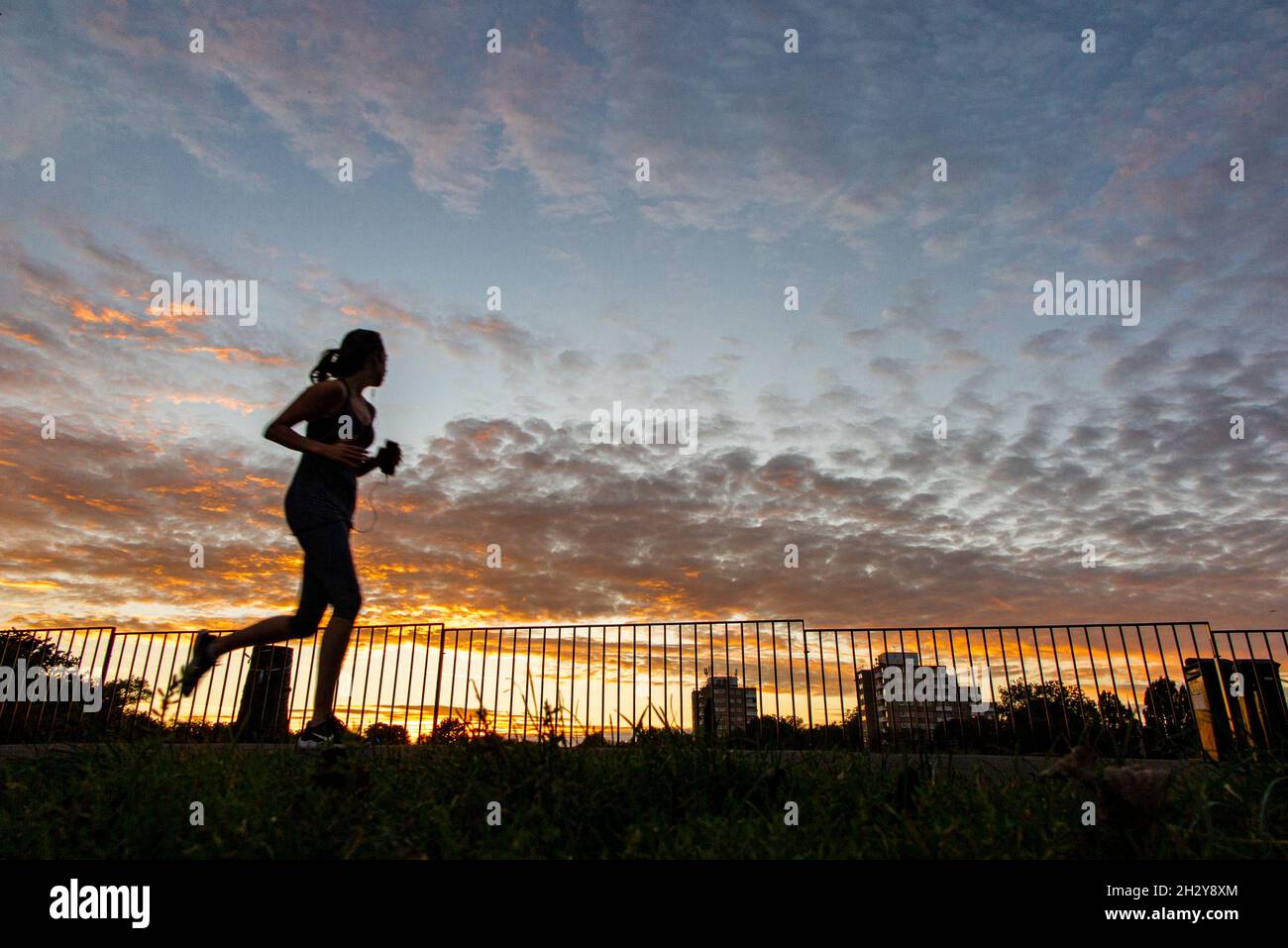 Running as the sun sets in an urban park in London with a tower block in the distance Stock Photo