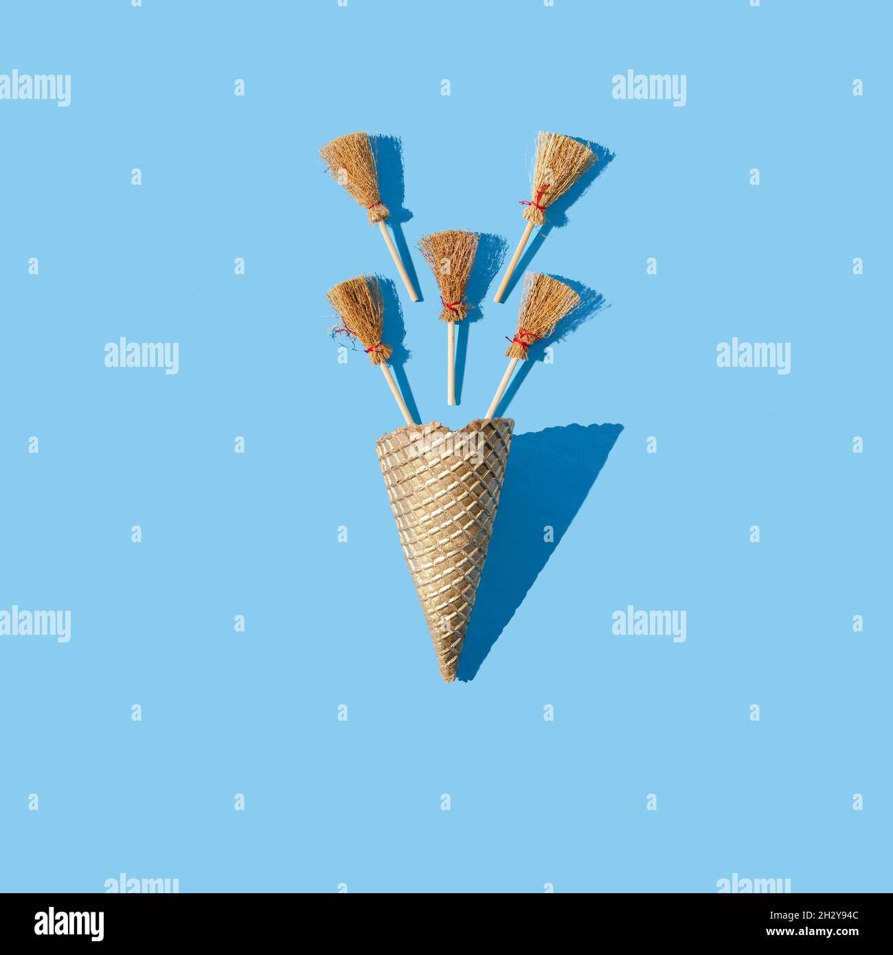 Five small brooms coming out of a golden ice cream cone on a pastel