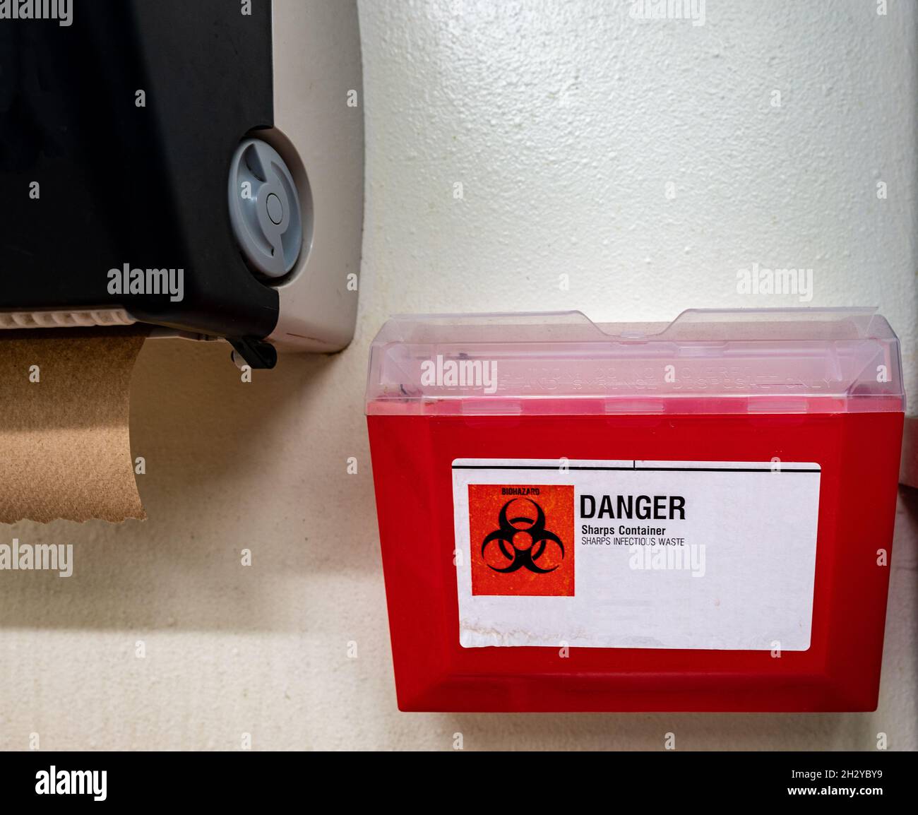 Red biohazard sharps waste container mounted to the wall of a public