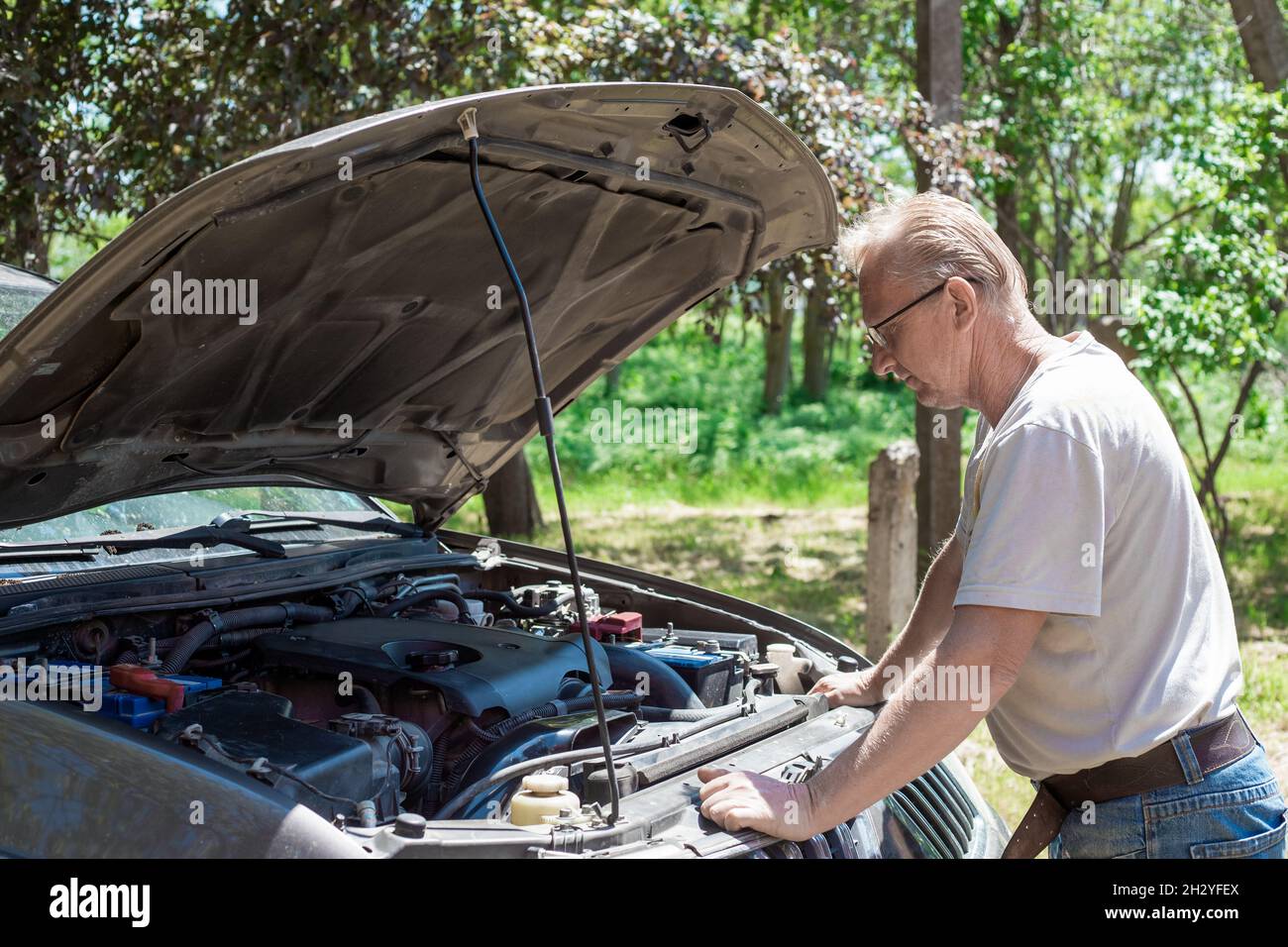 mature man bent over the open hood of a broken car. Repair and maintenance  of transport Stock Photo - Alamy