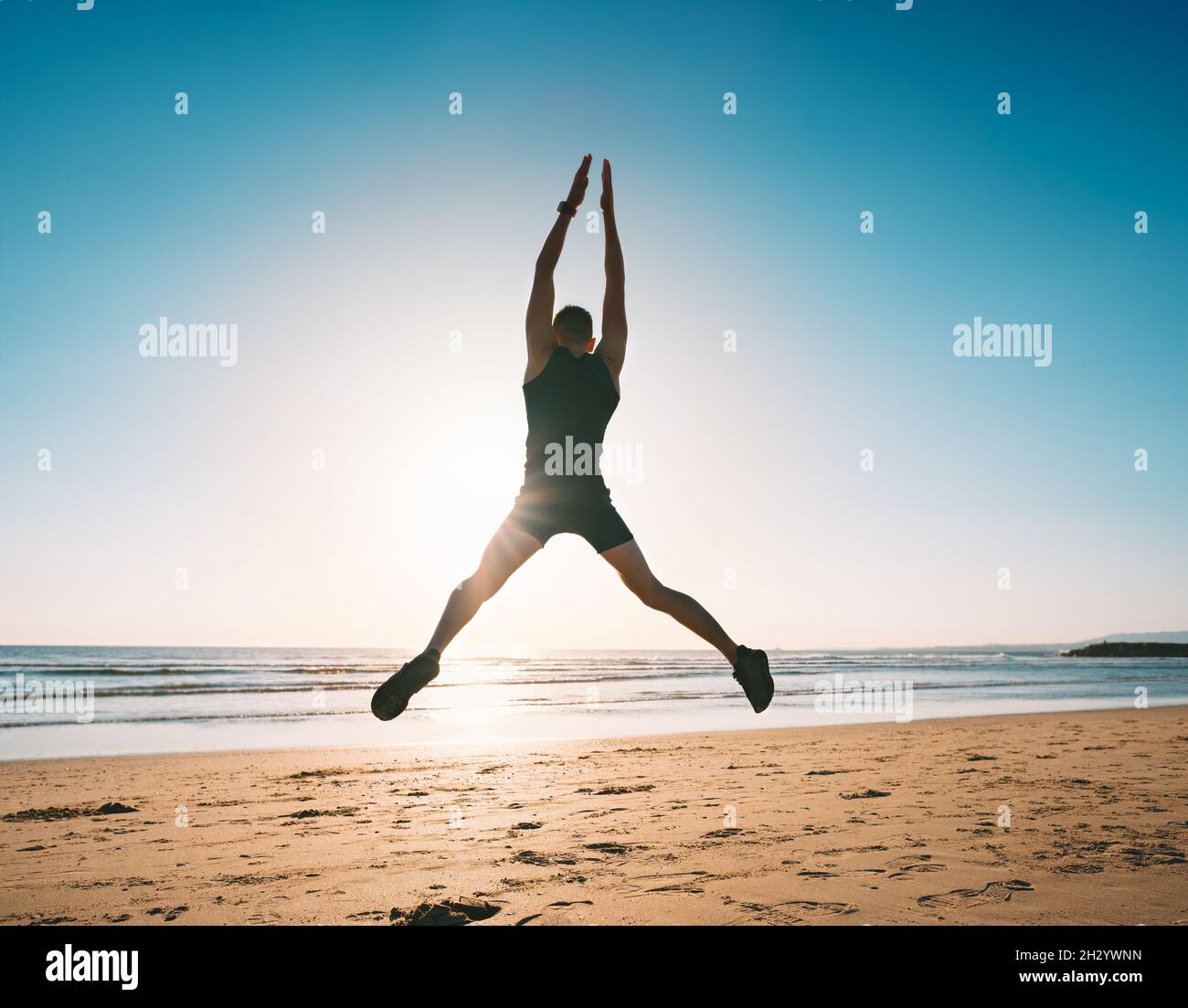 Jumping man. Young fitness man doing jumping jacks or star jump exercise on the beach Stock Photo