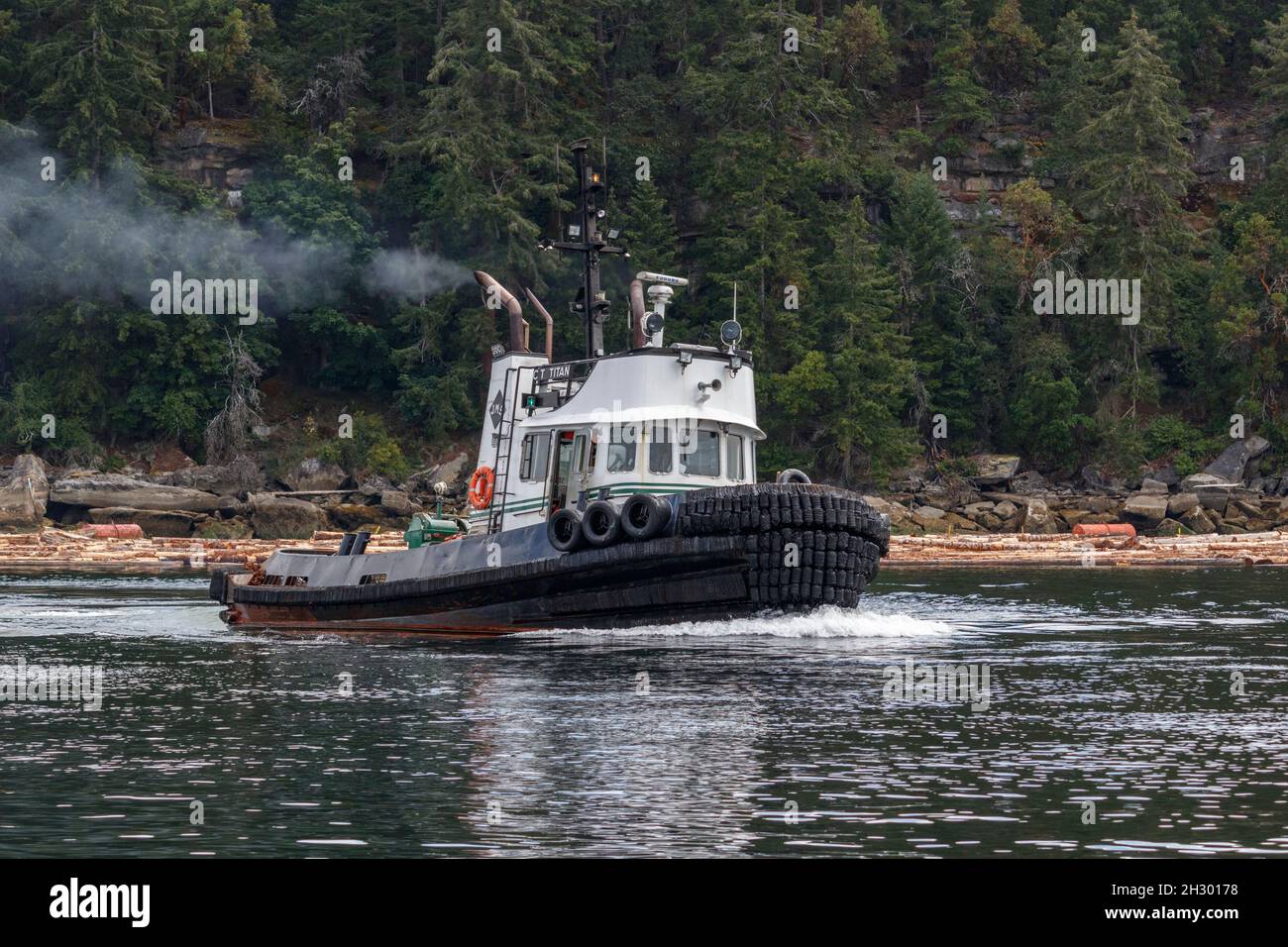 The tugboat CT Titan, working quickly to maneuver log booms off Valdes Island, produces a bow wave and exhaust plume as it moves away from shore. Stock Photo