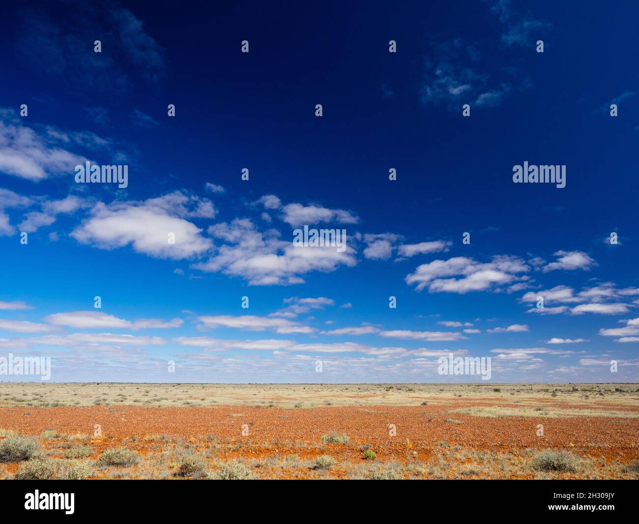 Red dirt and blue skies of the South Australian desert north of Coober Pedy seen from the Stuart Highway. Stock Photo