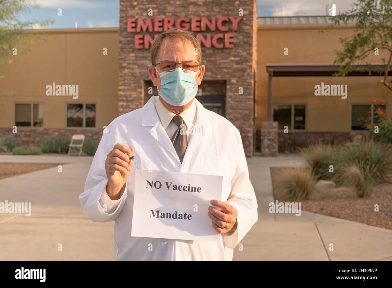 Angry doctor in white coat and mask holds injection and no vaccine mandate sign Stock Photo