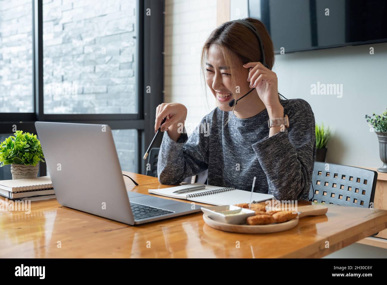 Happy asian woman freelancer wearing headset, communicating with client via video computer call. Millennial pleasant professional female tutor giving Stock Photo