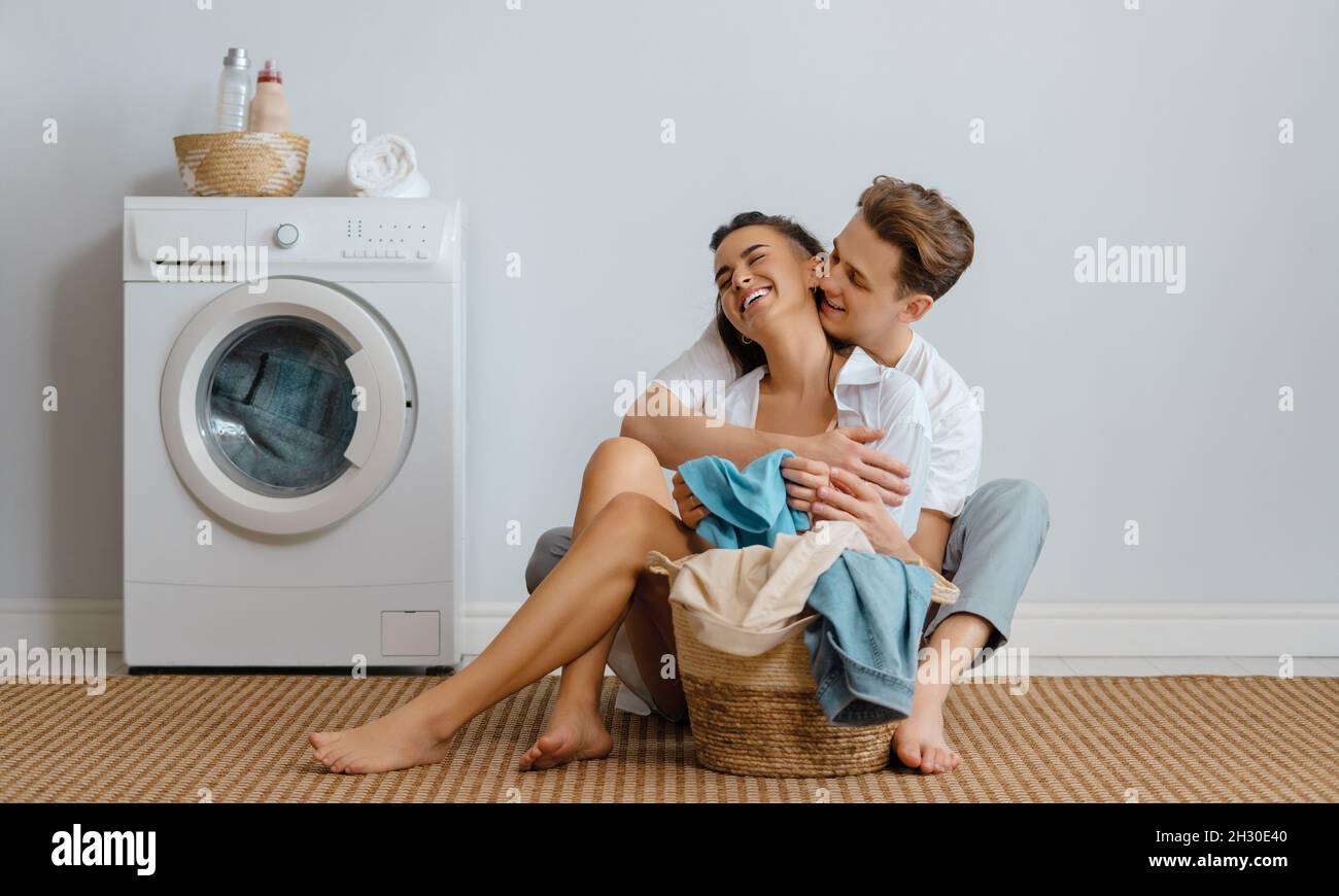 Beautiful young loving couple is smiling while doing laundry at home ...