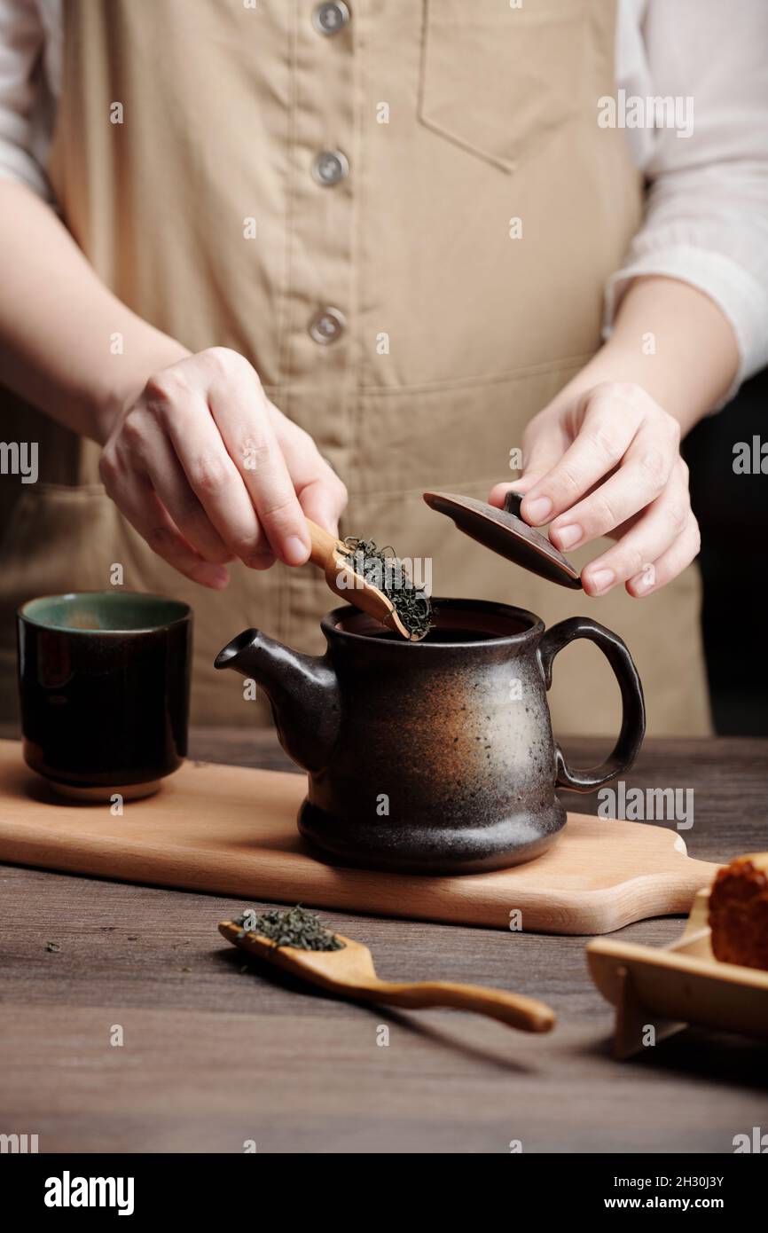 Hands of man steeping tea in ceramic pot at kitchen table Stock Photo