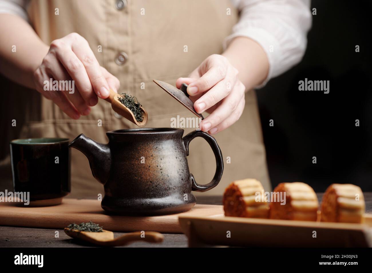 Close-up image of man putting spoon of dried tea leaves in ceramic pot Stock Photo