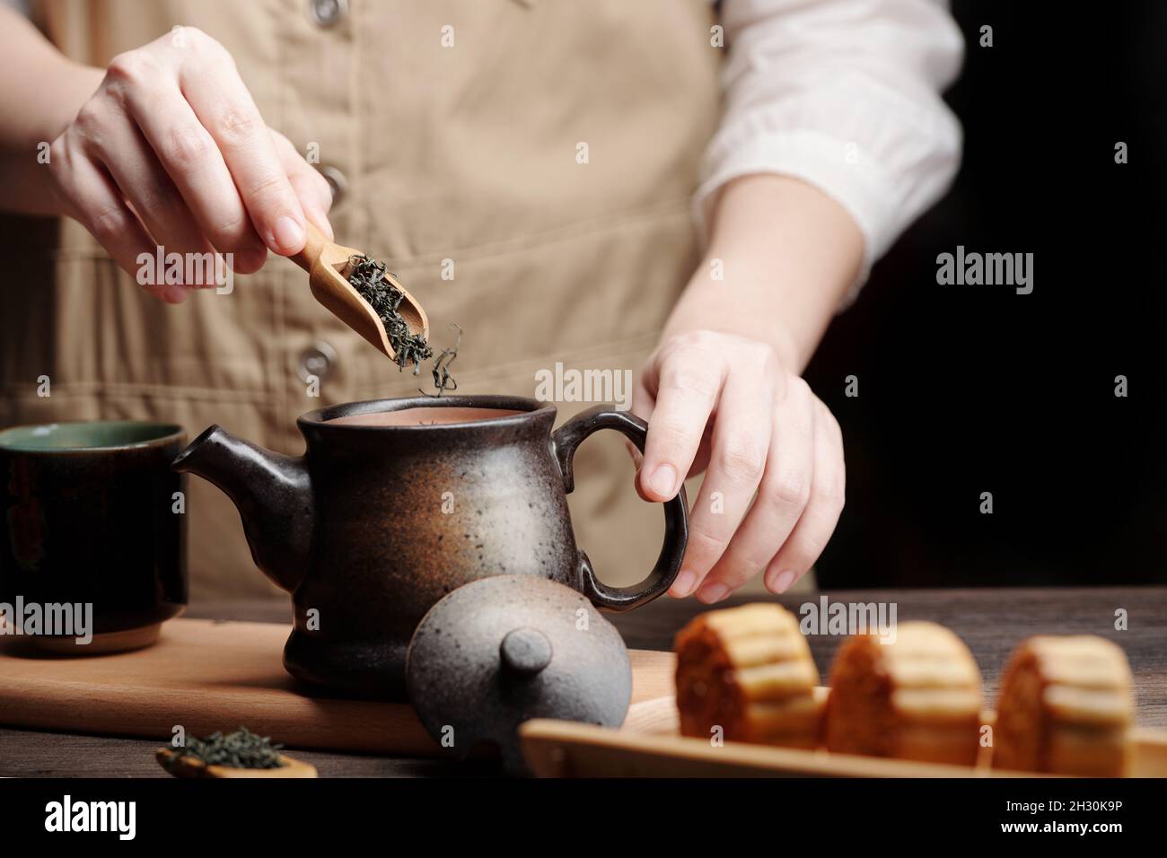 Man adding dried green tea leaves in ceramic pot when preparing drink for mid autumn festival Stock Photo