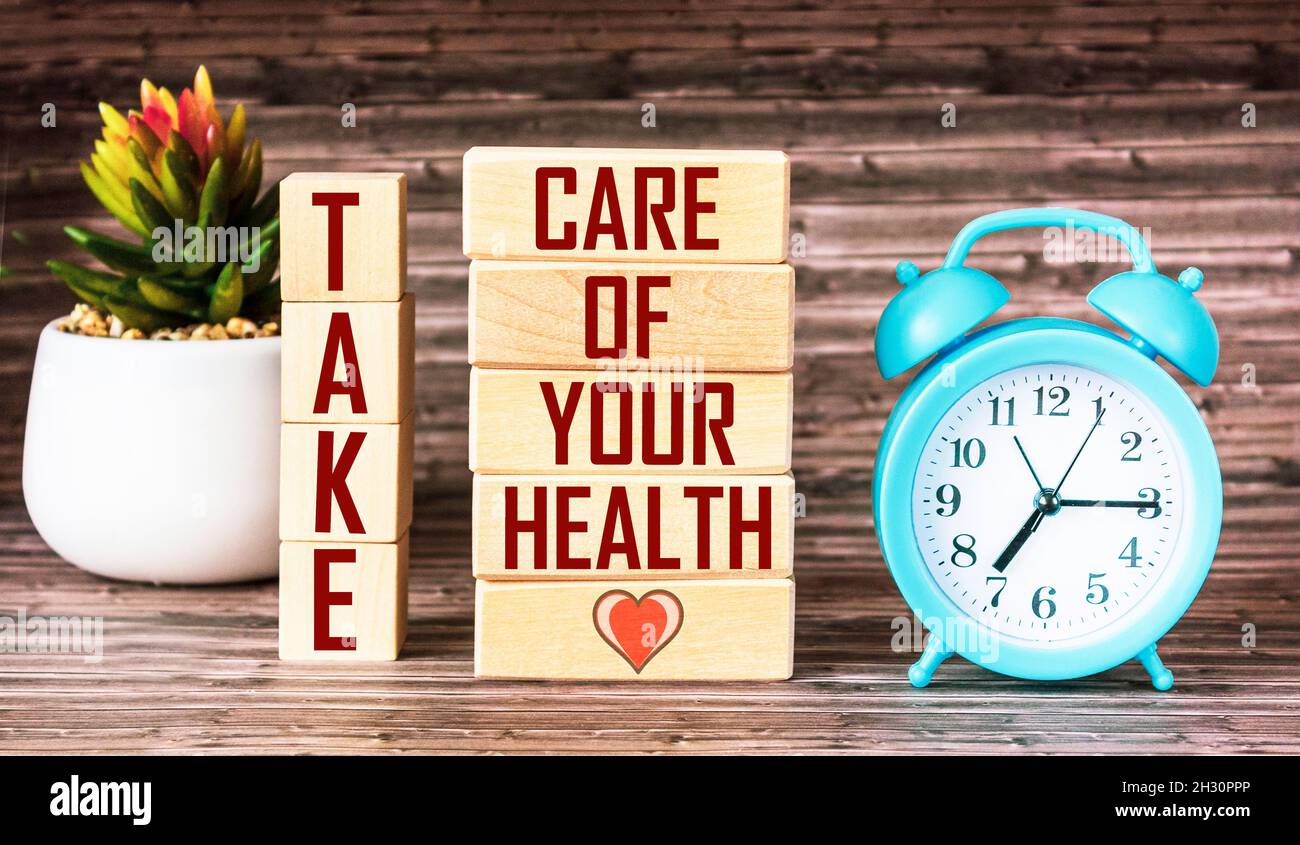 Take care of your health. The inscription is made on wooden blocks, next to a clock and a cactus flower on a wooden background Stock Photo