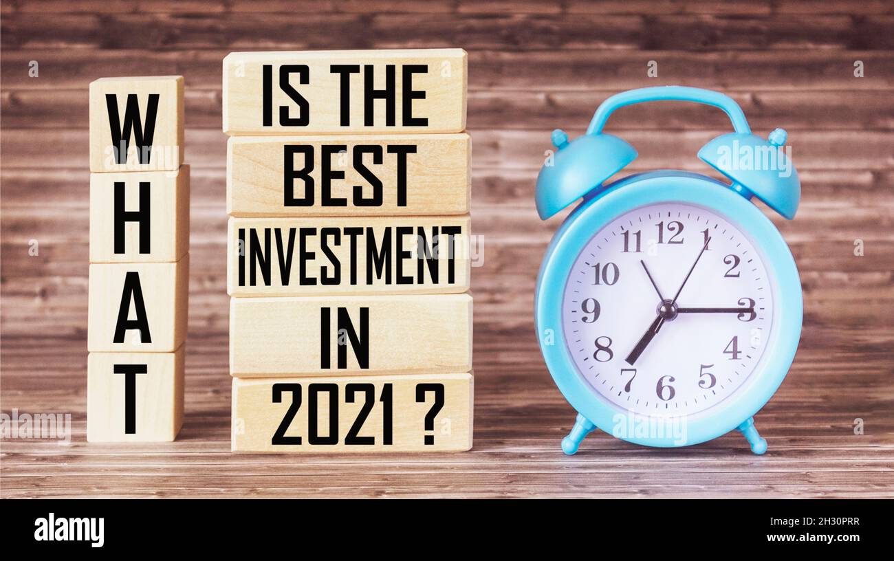Text What is the best investment in 2021 on wooden blocks and alarm clock on wooden background. Business concept. Stock Photo