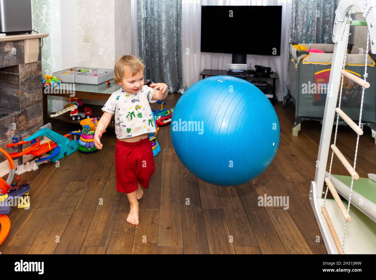 a little boy has fun and plays with a big blue ball fitball in the room