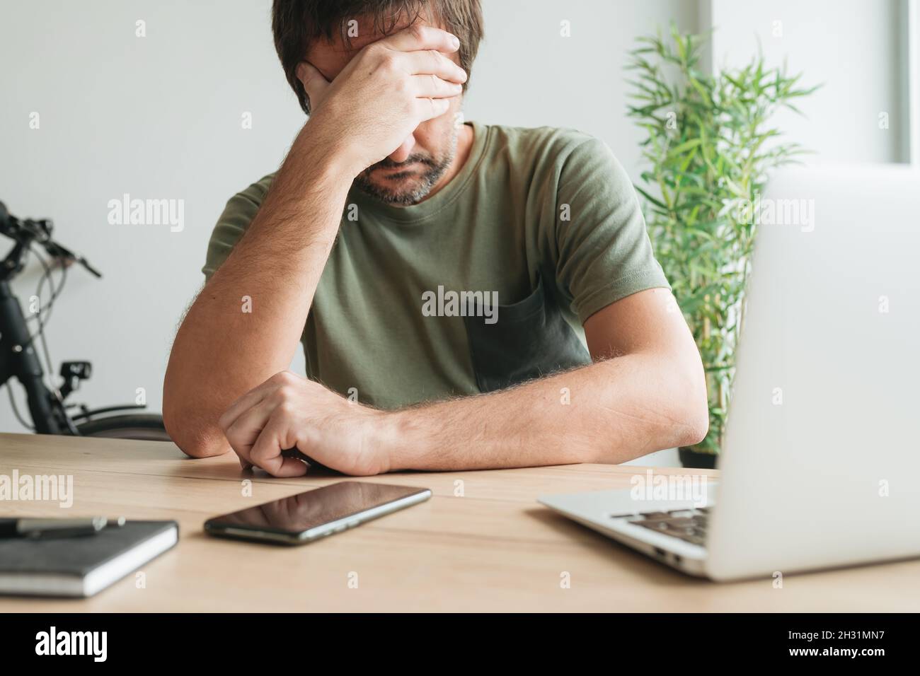 Disappointed telecommuter at home office desk covering face with his hand, selective focus Stock Photo