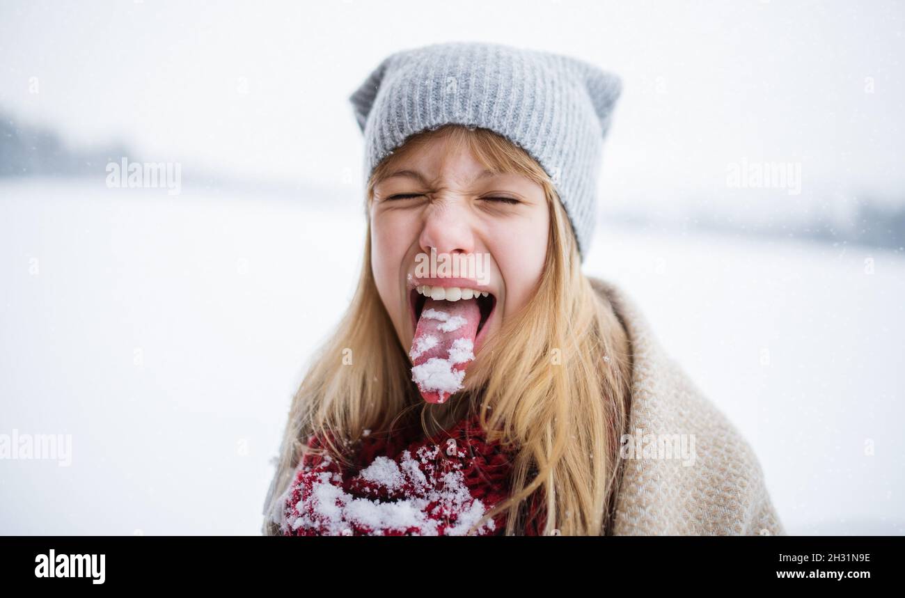 Headshot of happy preteen girl doing grimace and sticking tongue out with snow in winter nature Stock Photo