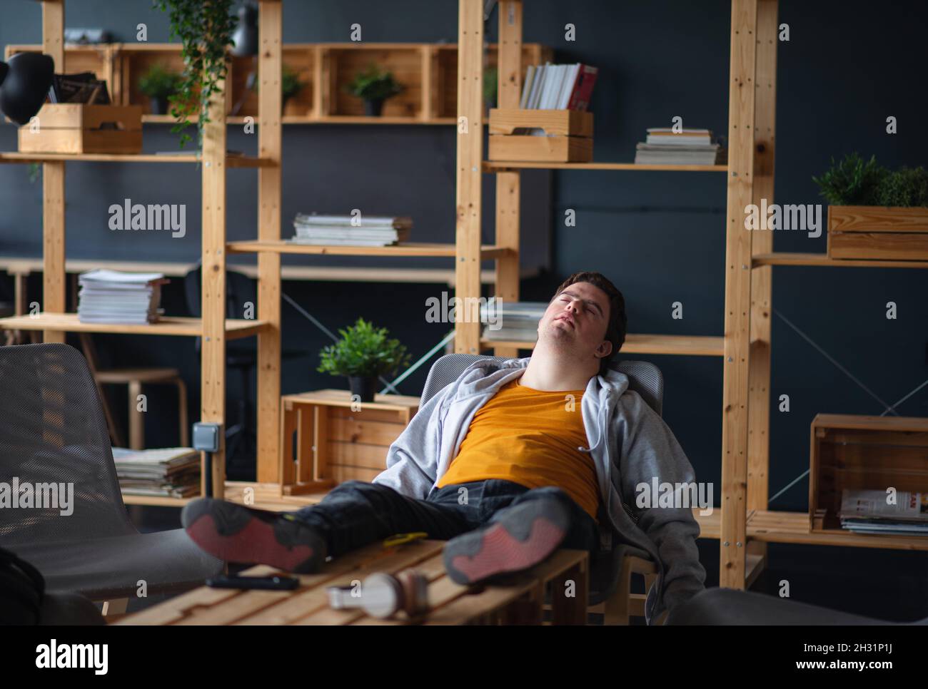 Young tired man with Down syndrome sitting indoors at school, taking break Stock Photo