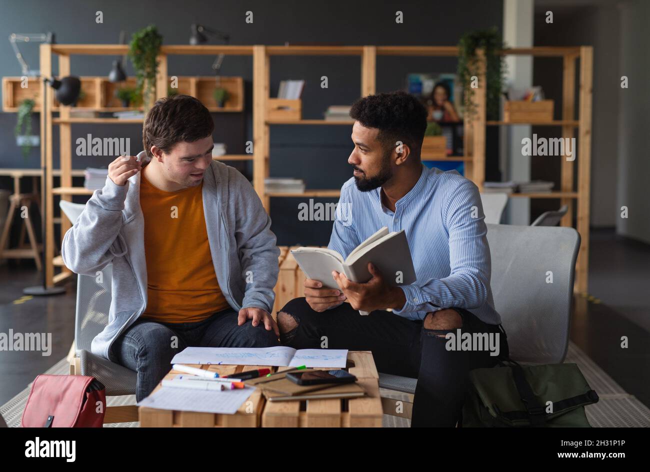 Young happy man with Down syndrome and his tutor studying indoors at school. Stock Photo