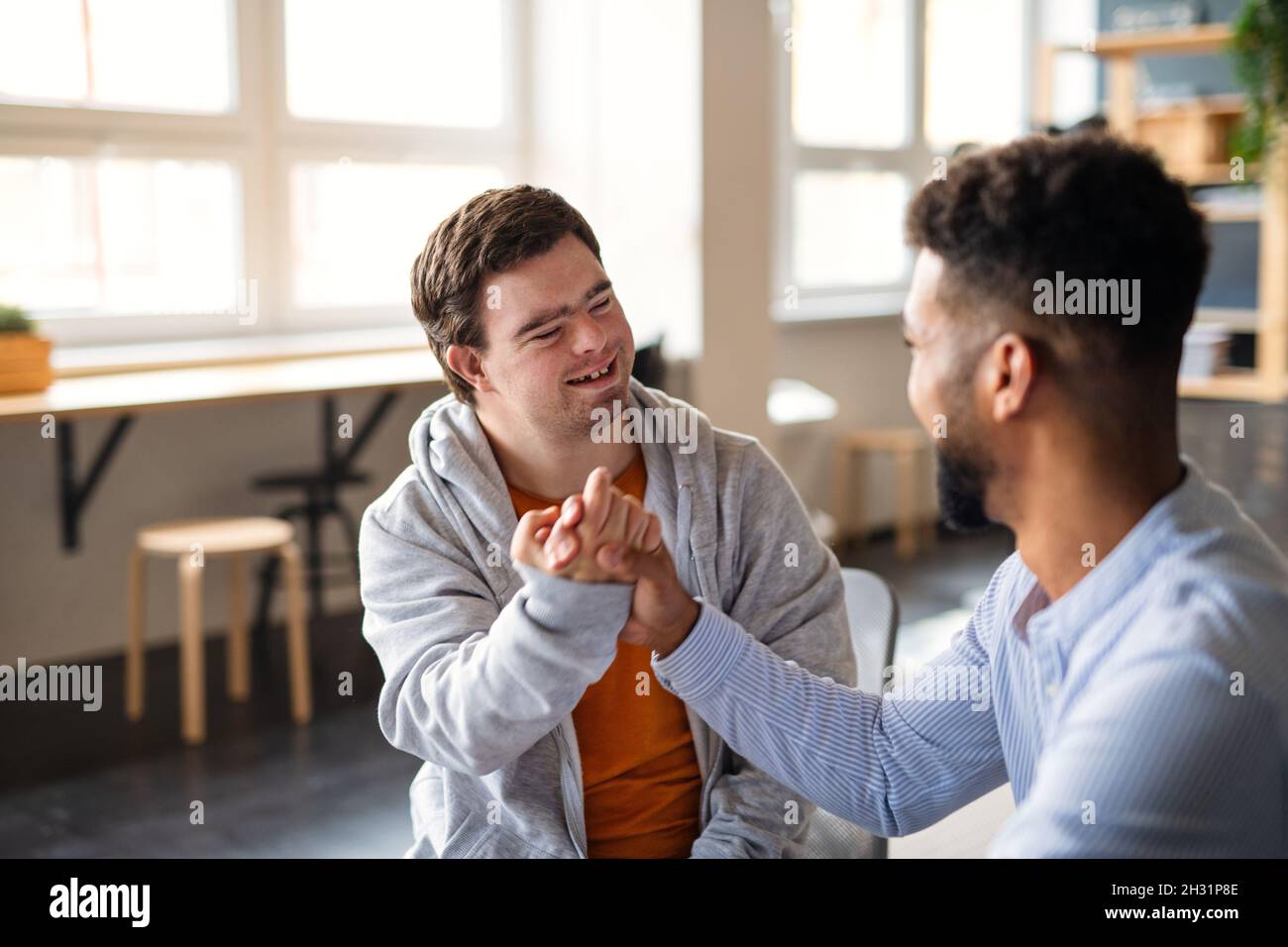 Young happy man with Down syndrome with his mentoring friend celebrating success indoors at school. Stock Photo