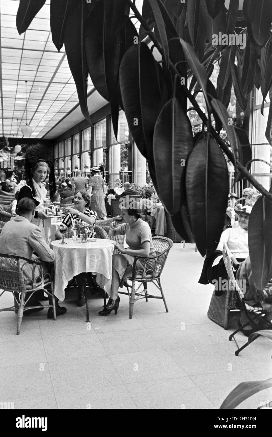 Besucher des Restaurants im Kurhaus Casino in Baden-Baden werden von Kellnerinnen bedient, die die traditionelle Schwarzwaldtracht mit dem Bollenhut tragen, Deutschland 1930er Jahre. Visitors of the restaurant in the Kurhaus Casino in Baden-Baden are being served by waitresses wearing a traditional Black Forrest costume with the Bollenhut, Germany 1930s. Stock Photo