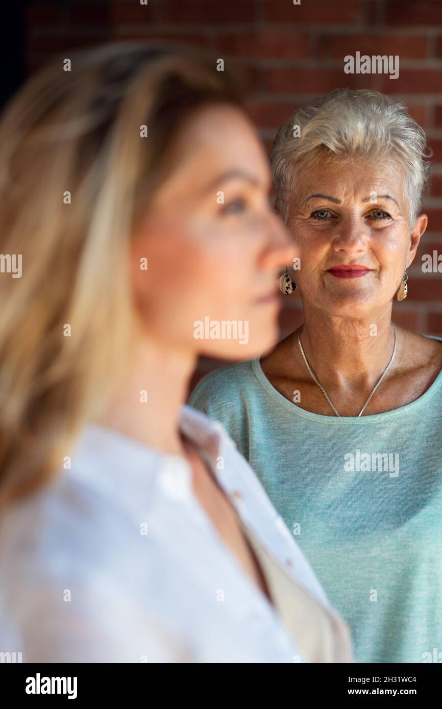 Senior mother looking at her adult daughter indoors at home. Selective focus on woman in background. Stock Photo