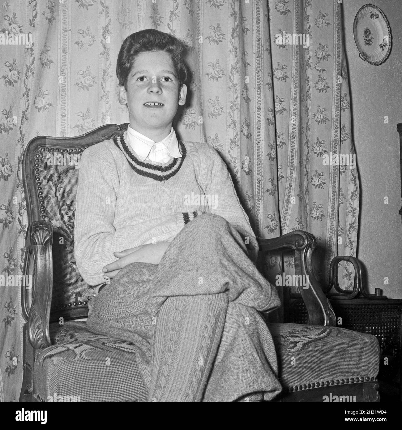 Ein Junge sitzt in Knickerbocker Hosen in einem Sessel im Wohnzimmer, Deutschland 1954. A boy wearing knickerbockers sitting in a chair at the living room, Germany 1954. Stock Photo