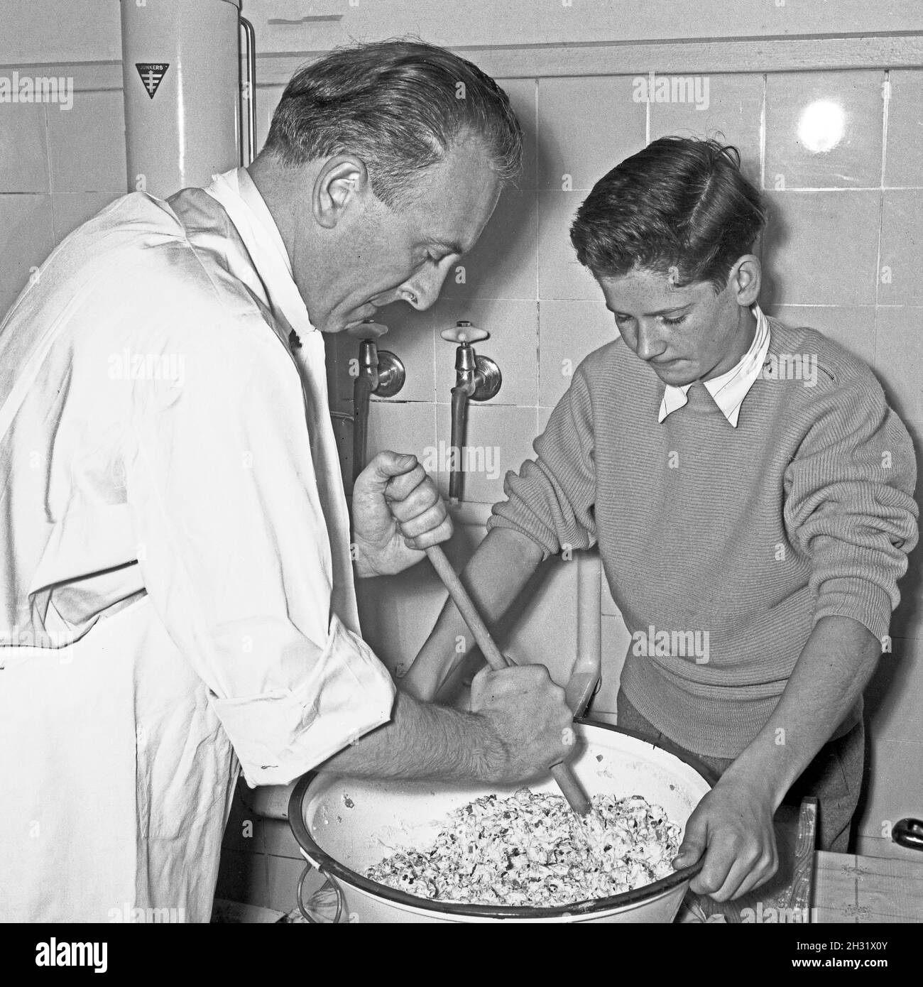 Der Schrecken der Hausfrau: Vater und Sohn bei der Zubereitung eines Nudelsalats, Deutschland 1958. Housewives in panic: father and son preparing a noodle salad, Germany 1958. Stock Photo