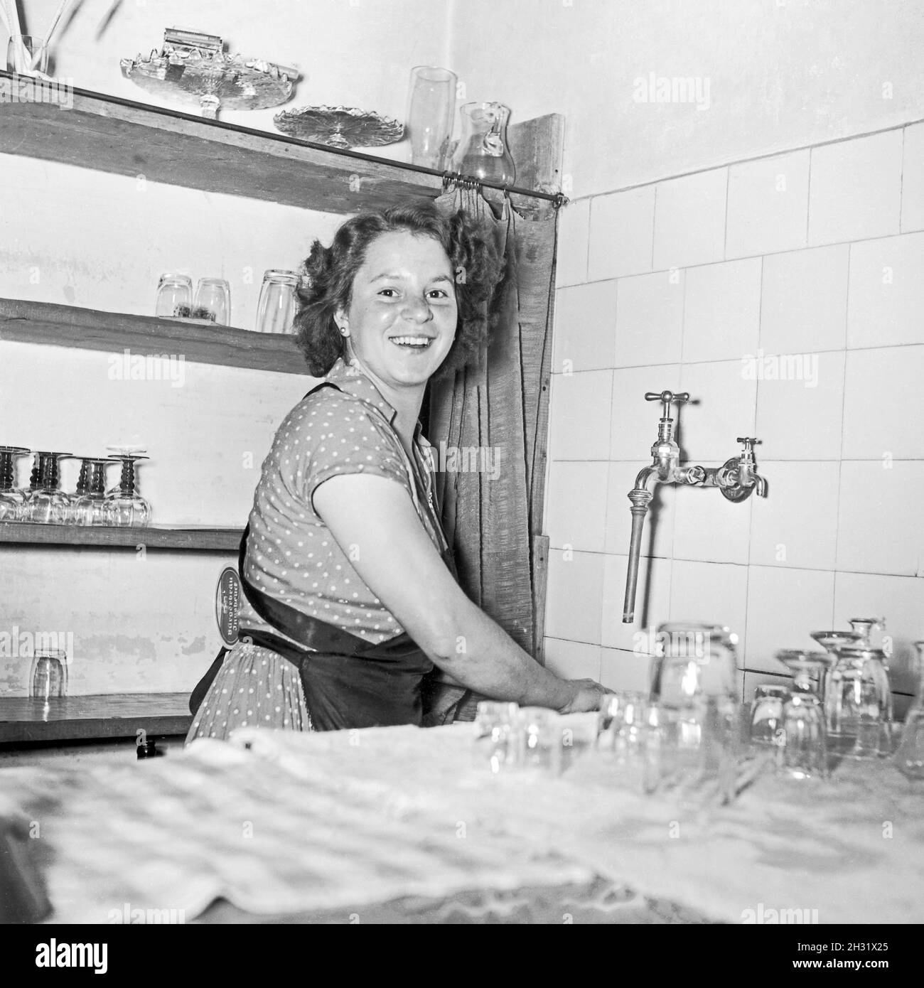 Junge Frau spült in der Küche im Gasthaus, Deutschland 1955. A young woman cleaning the glasses in a pub, Germany 1955- Stock Photo