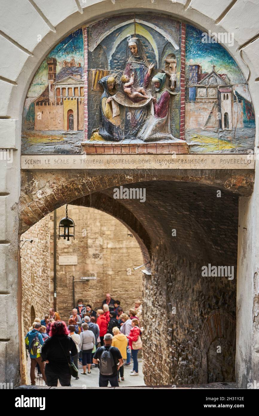 Torbogen mit Relief und Treppe zu dem Geburtshaus des heiligen Franziskus, Gruppe von Touristen oder Pilgern, Corso Manzini, Assisi, Umbrien, Italien Stock Photo