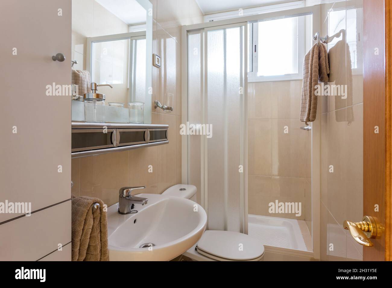 Simple style interior of small restroom with beige ceramic tile walls, white sink, classic WC toilet and shower cabin. Stock Photo