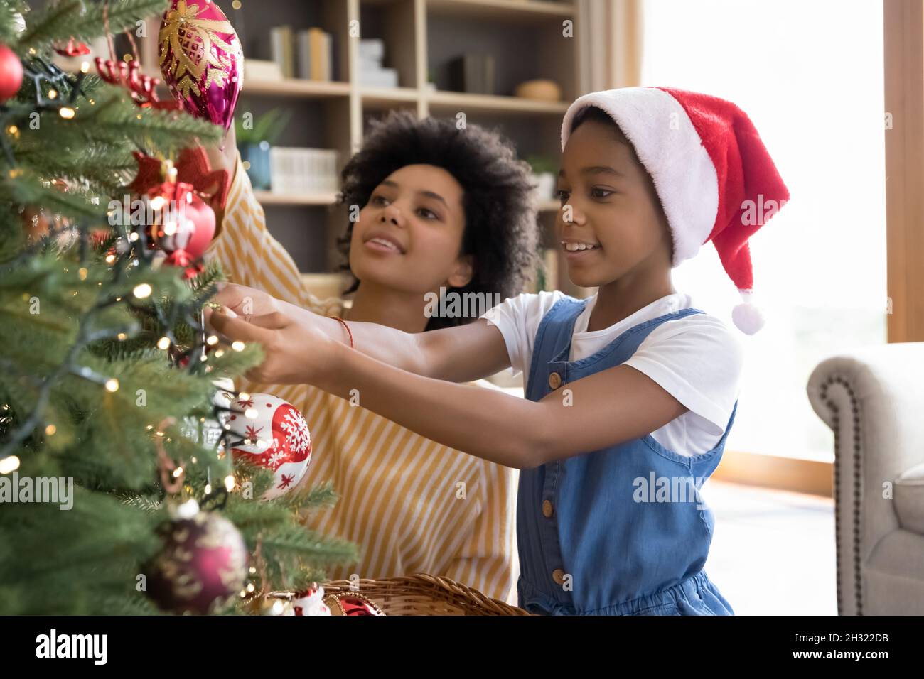 Happy little african kid girl decorating Christmas tree with mum Stock ...