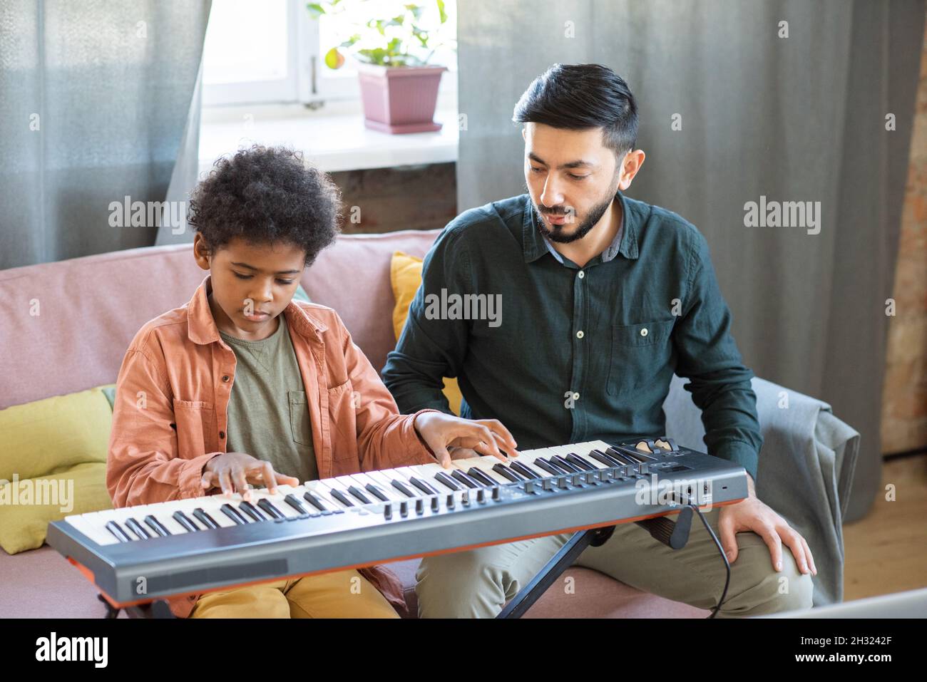 Cute schoolboy pressing keys of piano keyboard with his teacher sitting