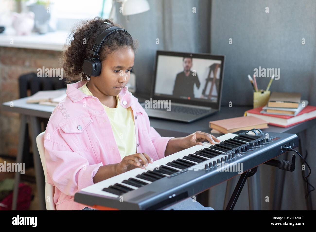 Pretty schoolgirl in headphones playing piano keyboard while
