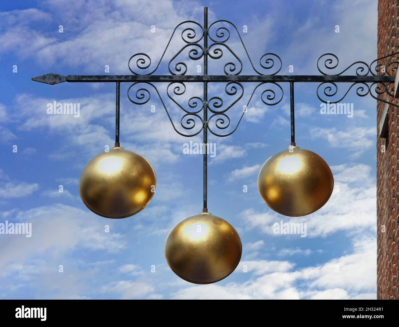 Pawn shop close up traditional sign three gold balls above Pawnbroker shop premises supported on ornamental iron bracket on a blue sky day England UK Stock Photo