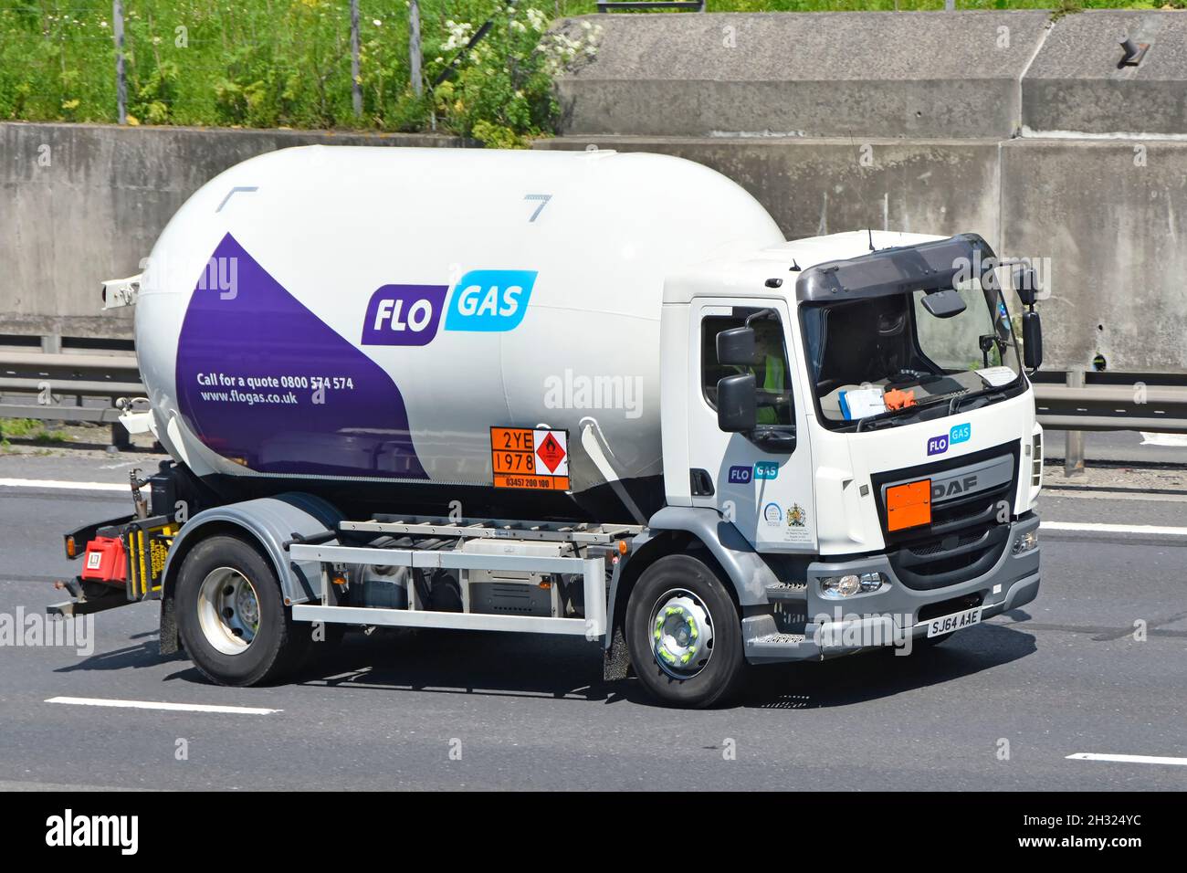 Side & front view short wheel base Flo Gas DAF mini tanker lorry truck & driver cab on motorway displays Hazchem Hazardous Chemicals sign England UK Stock Photo