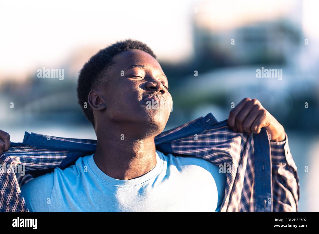 Young african man taking a sunbath while taking off the t-shirt outdoors Stock Photo