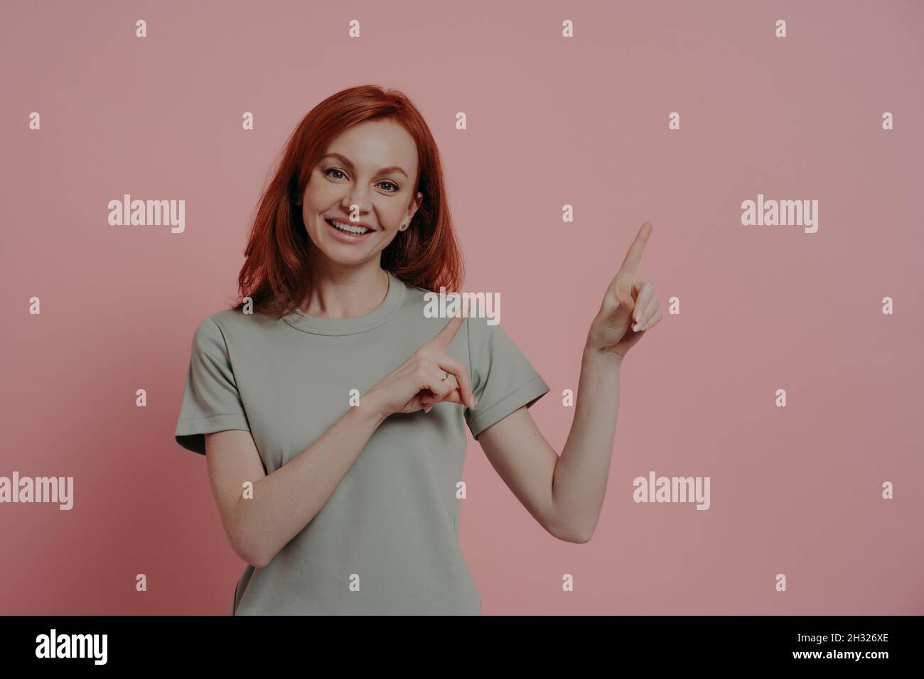 Satisfied pleased young redhead woman promoting product, pointing with index fingers at copy space Stock Photo