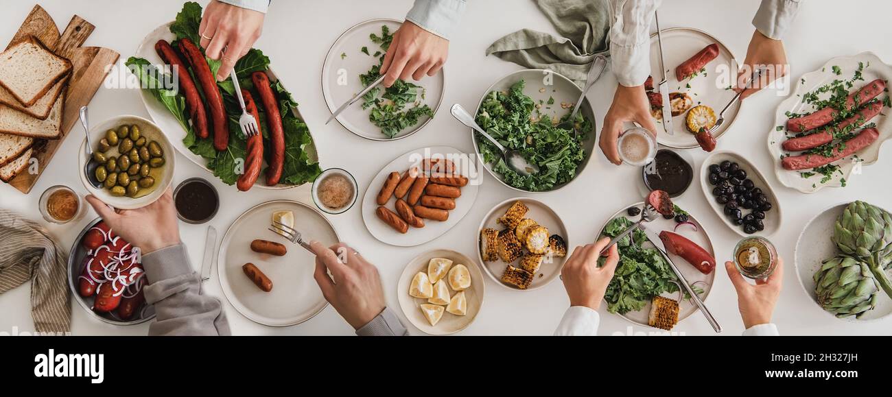 Flat-lay of hands eating pork sausages and snacks, holding beer Stock Photo