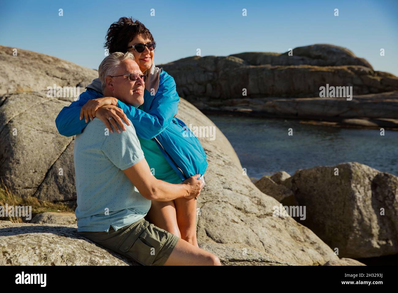 Loving mature couple traveling, sitting on the rock, exploring. Real man and woman hugging, kissing, Happily smiling. Scandinavian landscape, Norway Stock Photo