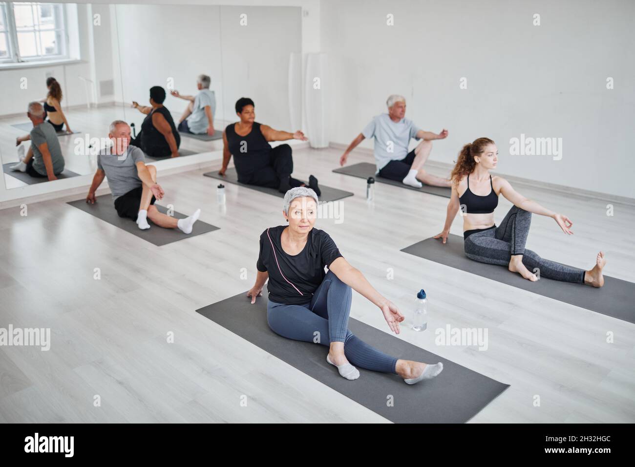 Group of people sitting on the floor on mats and exercising while practicing yoga in class Stock