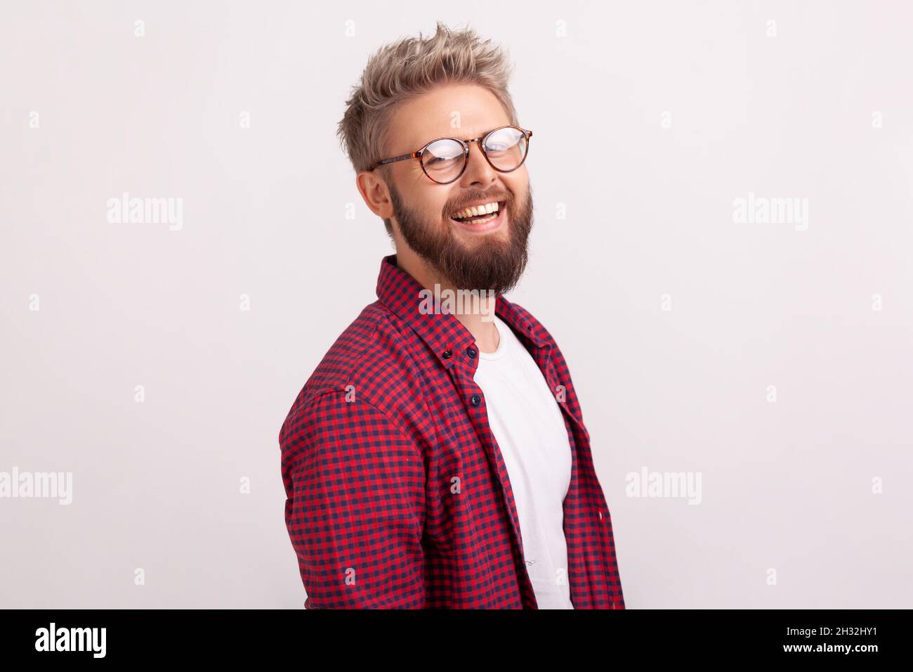 Side view portrait of joyful bearded blond guy in eyeglasses and casual clothes sincerely smiling looking at camera, good mood. Indoor studio shot isolated on gray background Stock Photo