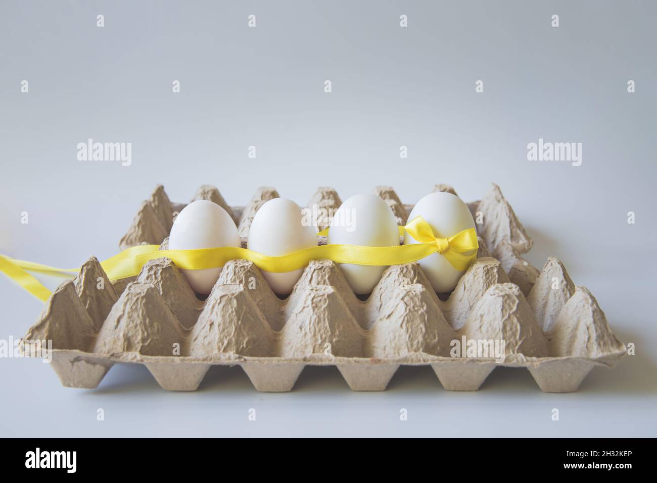 White eggs with yellow gift ribbon in an egg carton on a white background. Stock Photo