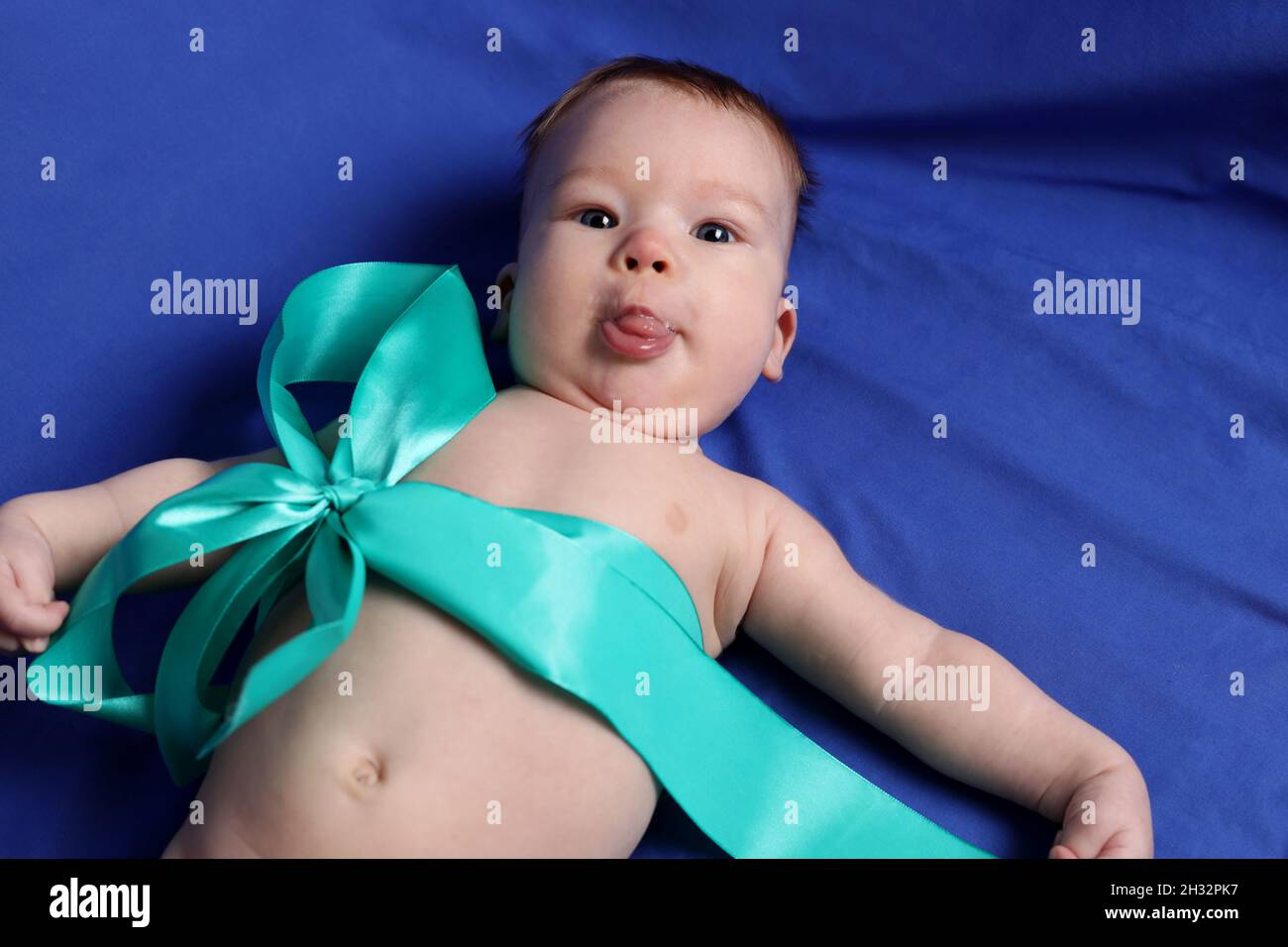 Little boy on the blue bed cover puts out tongue Stock Photo
