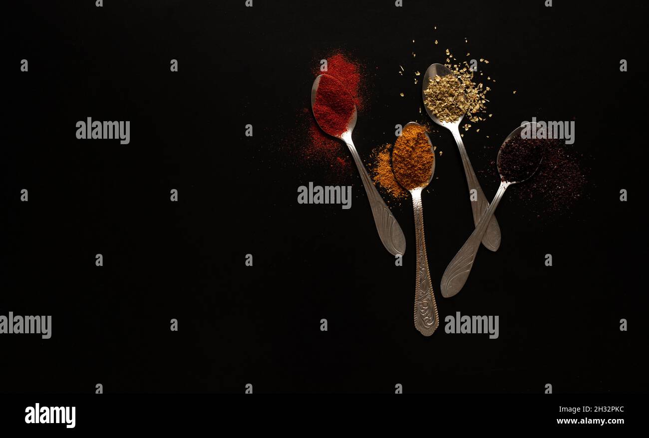Different spices in spoons on black background Stock Photo